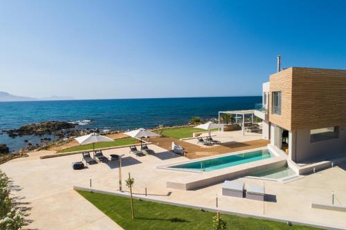 a house with a swimming pool next to the ocean at An intimate Villa Resort- Right on the beach, by ThinkVilla in Petres