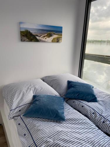 a bed with two blue pillows in front of a window at Ostsee Hausboot Schleswig Ostseeblick 1 in Schleswig