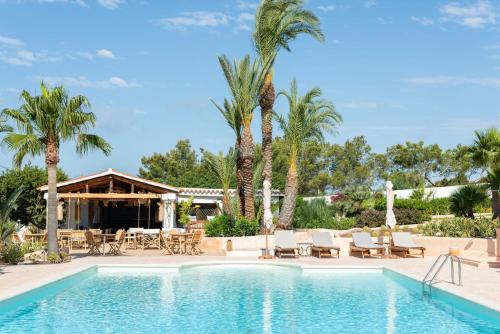 a swimming pool with chairs and a table and palm trees at Petunia Ibiza, a Beaumier hotel - Adults Only in Cala Vadella