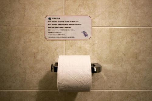a toilet paper dispenser in a bathroom with a sign at Hotel Irene City in Seoul
