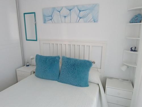 Una cama blanca con dos almohadas azules. en Apartamento El Príncipe en Peñíscola