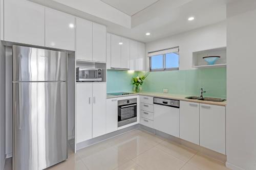 a kitchen with white cabinets and a refrigerator at Coco Mooloolaba in Mooloolaba