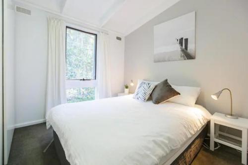 a white bedroom with a large bed and a window at Sandpiper On Smiths Lake in Smiths Lake