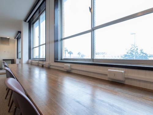a long table with chairs in a room with large windows at Tabist Hotel Miyakonojo Miyazaki in Miyakonozyō