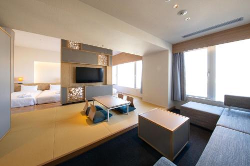 Habitación de hotel con cama, sofá y TV en AMANEK Beppu YULAｰRE en Beppu