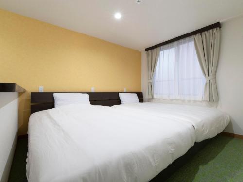 a bedroom with two white beds and a window at Tabist Hotel Miyakonojo Miyazaki in Miyakonozyō