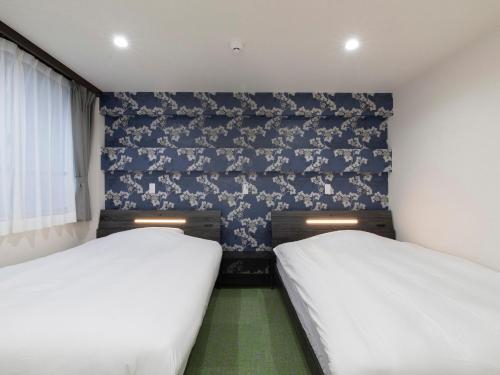 two beds in a small room with blue wallpaper at Tabist Hotel Miyakonojo Miyazaki in Miyakonozyō