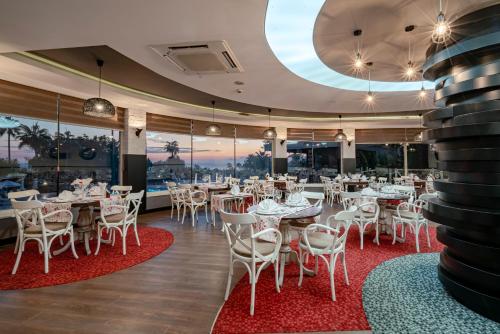 a restaurant with white tables and chairs and a large window at Iz Flower Side Beach Hotel in Side