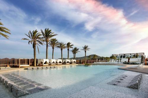 une grande piscine avec des chaises et des palmiers dans l'établissement Hard Rock Hotel Ibiza, à Playa d'en Bossa