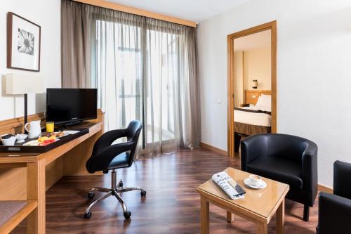 a hotel room with a desk and chairs and a bedroom at Rafaelhoteles Piramides in Madrid