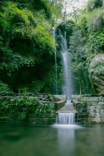 a waterfall in the middle of a body of water at Rustic wood house - A village home stay in Jibhi Valley in Jibhi