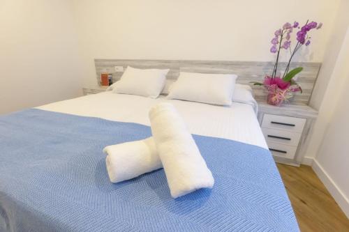 1 cama con 2 almohadas blancas y manta azul en Apartamentos Centro Llanes, en Llanes