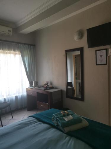 a bedroom with a bed and a desk and a mirror at Klyne Jiweel Guesthouse in Pretoria