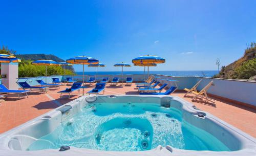 a hot tub on a patio with chairs and umbrellas at Hotel Cava Dell'Isola in Ischia