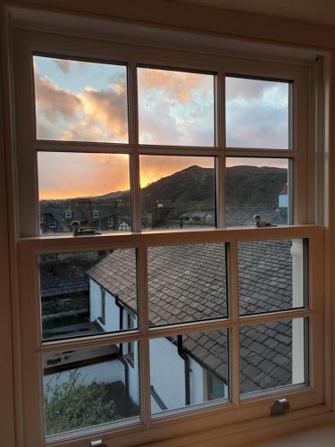 a window with a view of a sunset seen through it at Peggy Hill Cottage in Ambleside