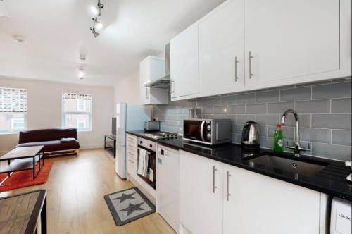 a kitchen with white cabinets and a living room at Modern split level 1 bedroom flat in Aldgate in London