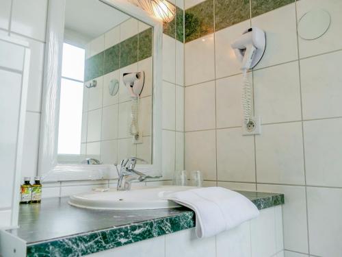 ein weißes Badezimmer mit einem Waschbecken und einem Spiegel in der Unterkunft Hotel Berlioz Basel Airport in Saint-Louis