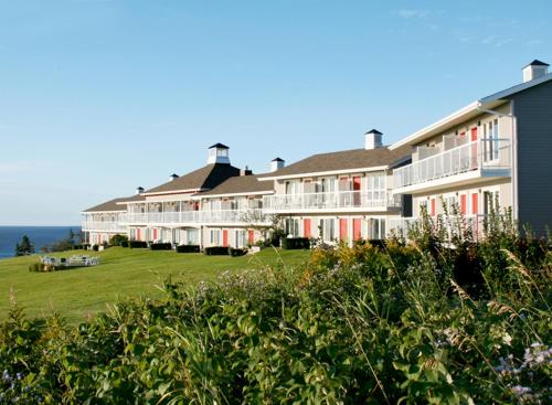 un gran edificio con ventanas rojas y blancas y el océano en Hôtel le Mirage, en Percé