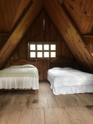 two beds in a wooden attic bedroom with a window at Cabañas Toniná Kayab in Ocosingo
