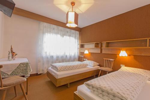 a bedroom with two beds and a table and a window at GARNI AQUILA in Corvara in Badia