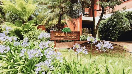a sign in a garden with purple flowers at Pousada Pinhão e Poesia in Canela