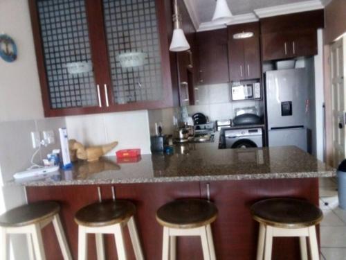 Una cocina con una encimera con cuatro taburetes de bar. en Cerf@BeachFront, en Margate