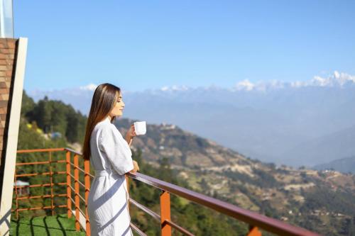 a woman standing on a balcony holding a cup of coffee at Hotel Mystic Mountain in Nagarkot