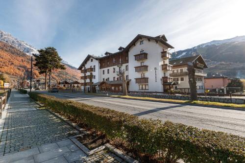 a large white building on a street with mountains in the background at Hotel Villa Rina in Bormio
