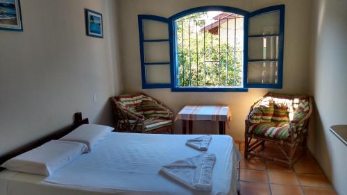 a bedroom with a bed and two chairs and a window at Pousada Canoeiro in Ubatuba