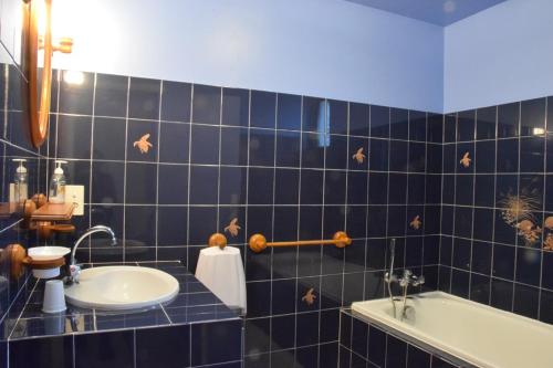 une salle de bain carrelée bleue avec un lavabo et une baignoire dans l'établissement La ferme des Cailloux, à Sassay