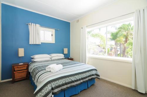 Dormitorio azul con cama y ventana en Jervis Bay Waterfront, en Vincentia