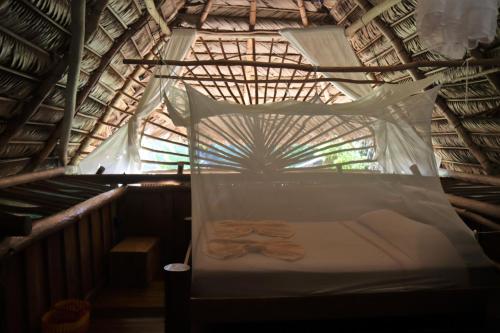 a bed in a thatched room with a net at El Hotelito Perdido in Rio Dulce