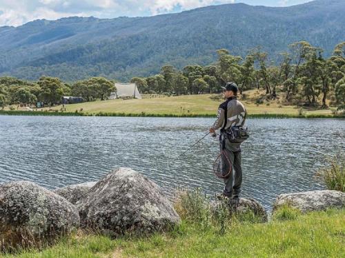 a man standing on rocks near a body of water at Stillwater Chalet B - Amazing Lakefront 2BR Chalet l BBQ l Gym l Tennis l Indoor Pool in Crackenback