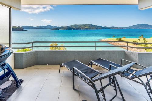 a balcony with chairs and a view of the water at Frangipani Apartments on Hamilton Island by HIHA in Hamilton Island