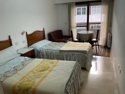 a room with two beds and a table and a window at RESIDENCIA UNIVERSIDAD in Ourense