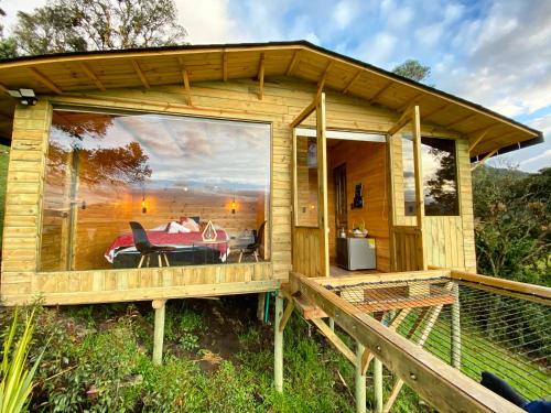 a wooden cabin with a large window on a deck at Neusa Hills Glamping in Tausa Viejo