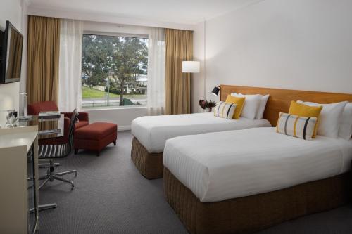 a hotel room with two beds and a desk at Rydges Bankstown in Bankstown