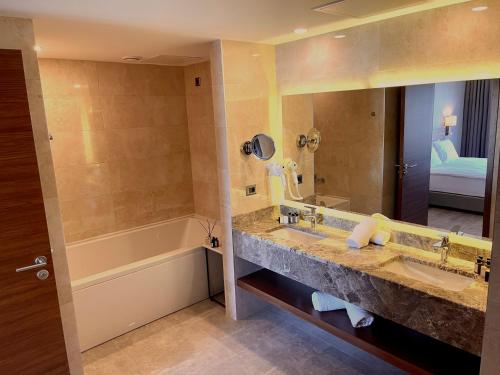 een badkamer met 2 wastafels, een bad en een spiegel bij Türkmen Riverside Hotel Adana in Adana