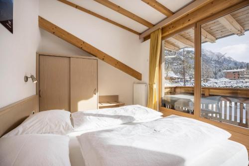 a bedroom with a white bed and a large window at Runcac Apt Gomina in San Vigilio Di Marebbe