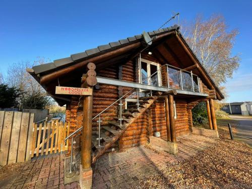a log cabin with a staircase in front of it at Woodpecker Log Cabin with hot tub, pizza oven bbq entertainment area, lakeside with private fishing peg situated at Tattershall Lakes in Tattershall