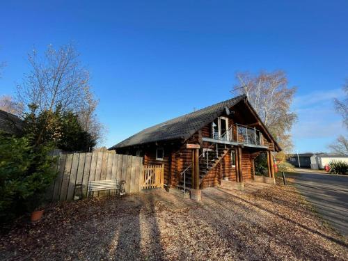 a log cabin with a fence in front of it at Woodpecker Log Cabin with hot tub, pizza oven bbq entertainment area, lakeside with private fishing peg situated at Tattershall Lakes in Tattershall