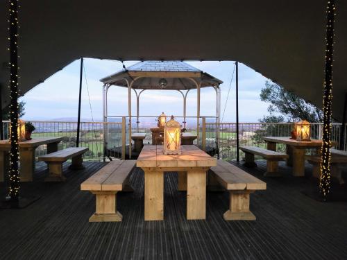 a wooden table with benches and an umbrella on a deck at Wheal Tor Hotel & Glamping in Liskeard