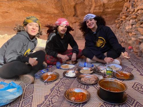 grupa trzech kobiet siedzących przy stole z jedzeniem w obiekcie Wadi Rum Cave Camp &Jeep Tour w mieście Wadi Rum