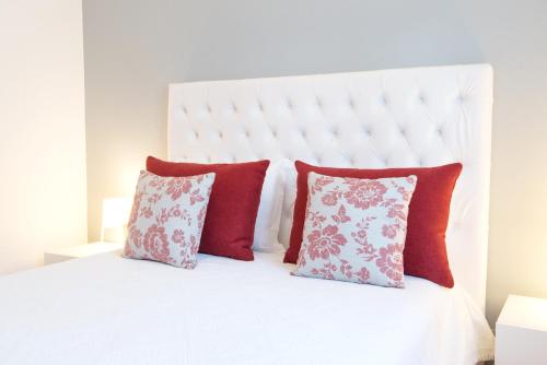 a white bed with red pillows and a white headboard at Casas da Vila - Duna Parque Group in Vila Nova de Milfontes