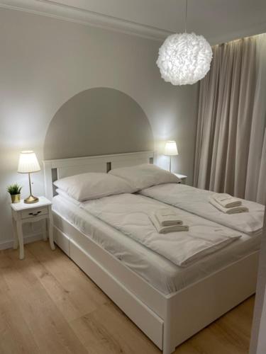 - une chambre blanche avec un grand lit et un lustre dans l'établissement Apartament Premium IV z Garażem, à Kołobrzeg