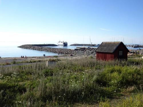 a red shack on a beach with a boat in the water at 1B, Stuga m havsutsikt & 50m till strand in Byxelkrok