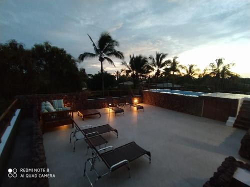 a patio with chairs and a swimming pool at sunset at Praia do Forte Ohana Residence in Praia do Forte