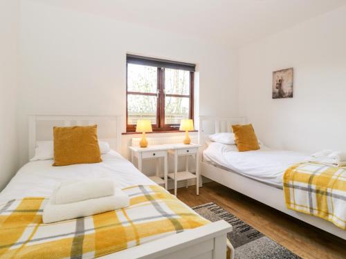 two beds in a white room with two lamps at Stable Cottage in Winscombe