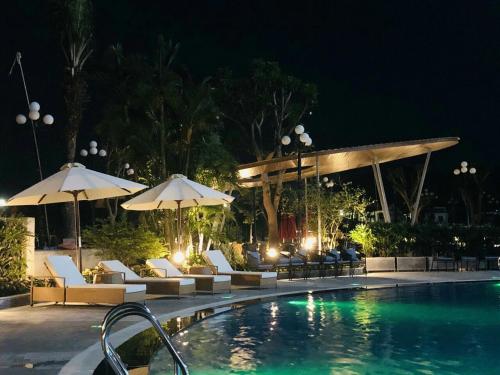 a swimming pool with chairs and umbrellas at night at Songlam Waterfront Hotel in Hà Tĩnh