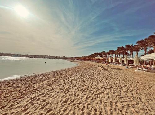 una playa de arena con sombrillas y sillas y el océano en Sunrise Tucana Resort Grand Select- en Hurghada